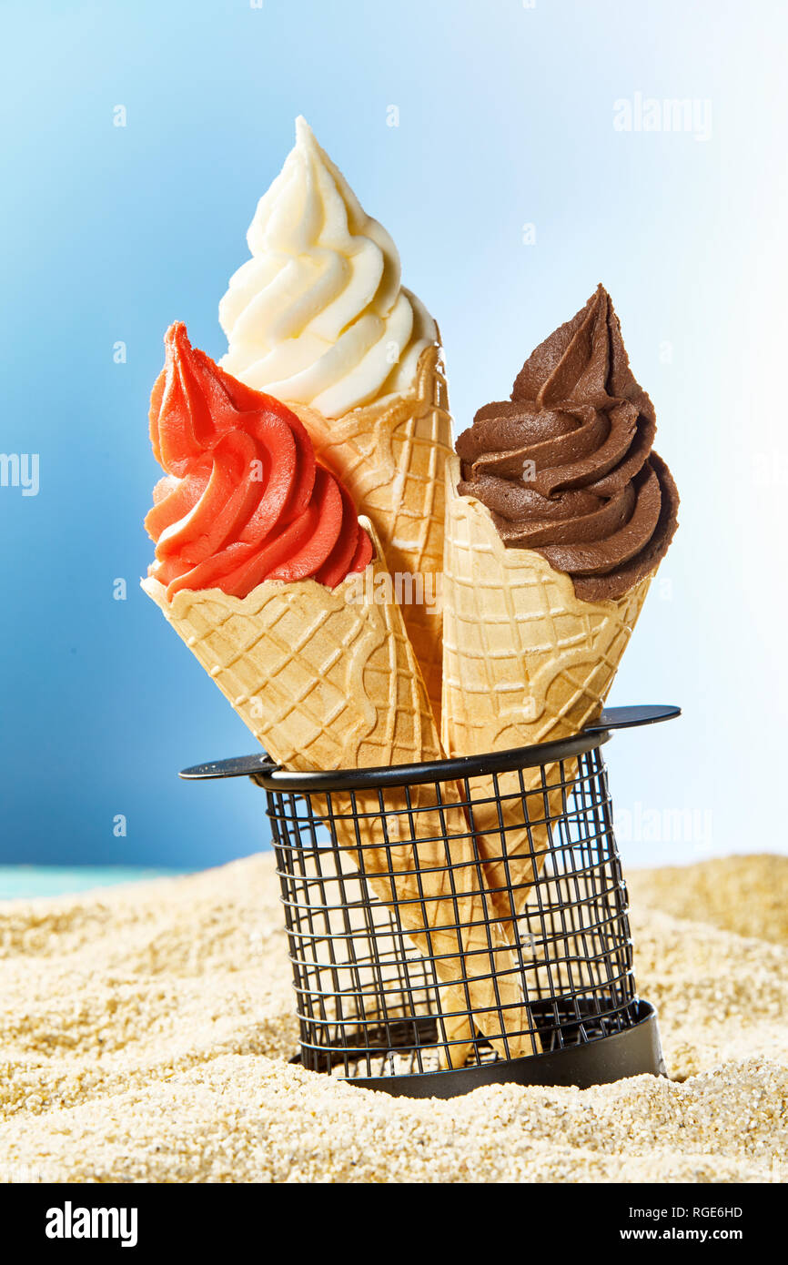 Three crispy cones with ice cream stuck in container on sandy beach