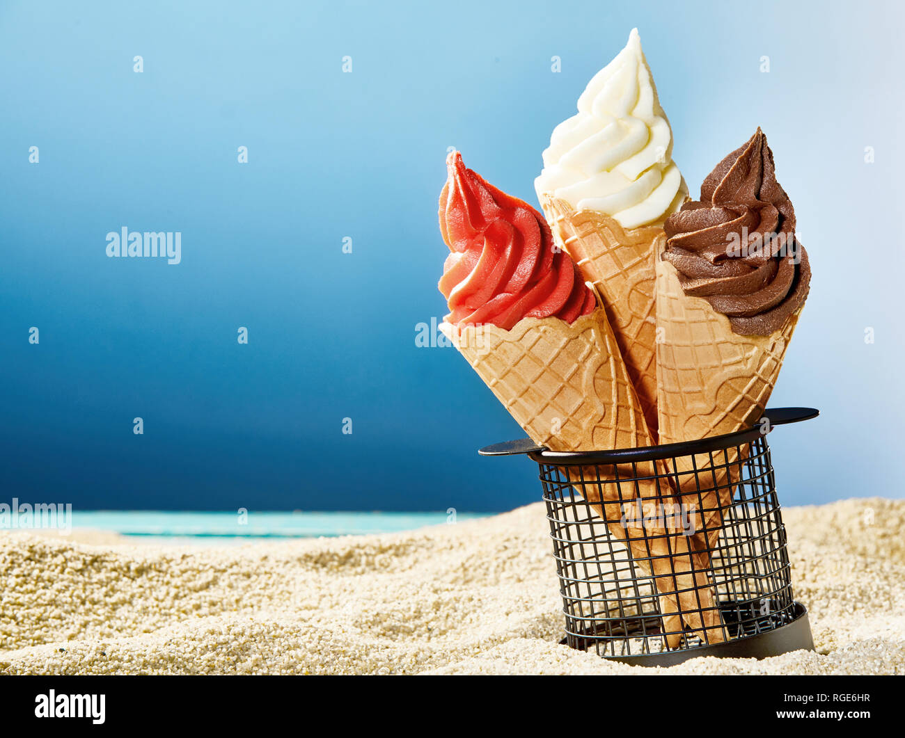 Three crunchy wafer cones with ice cream stuck in container on sandy