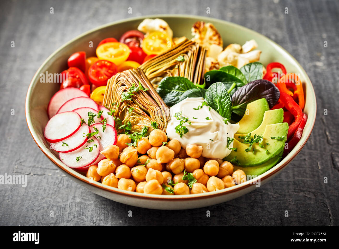 Colorful Buddha bowl with a variety of healthy fresh vegetables including chickpeas, avocado, radish, sweet pepper, tomatoes, cauliflower and artichok Stock Photo