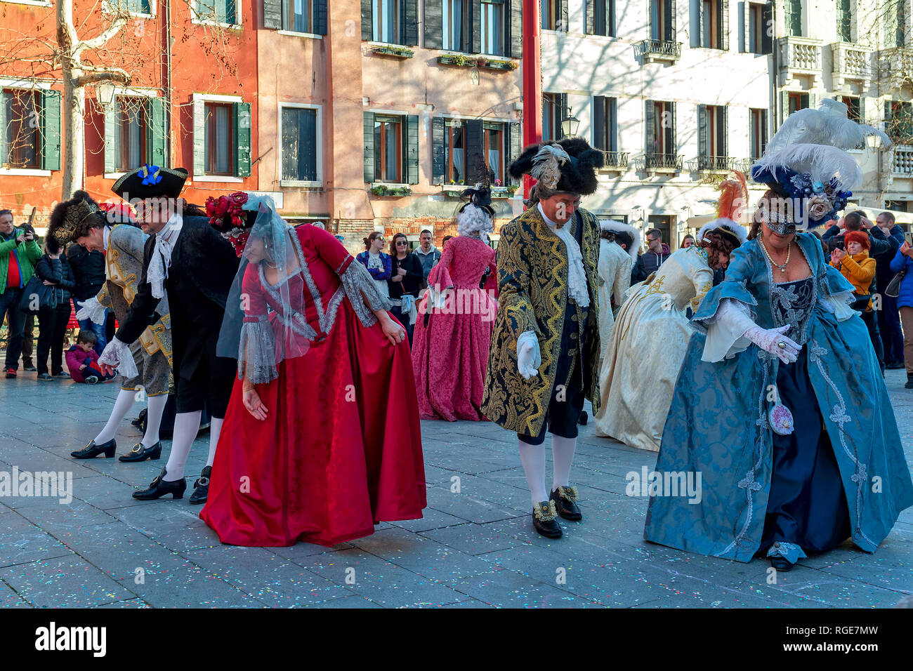 Group of people wearing typical costumes and masks dancing on small square during famous traditional annual carnival in Venice. Stock Photo