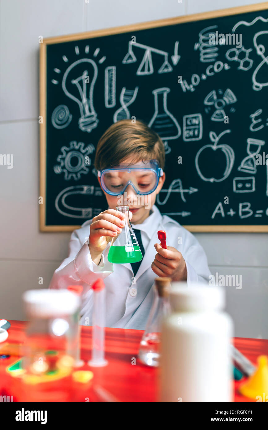 Boy dressed as chemist playing with chemistry game in front of a blackboard with drawings Stock Photo