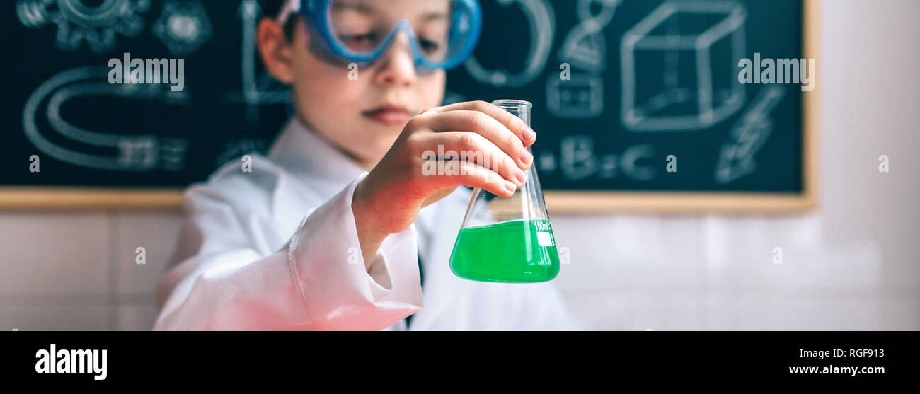 Little boy scientist with glasses holding flask with chemical green liquid against of drawn blackboard Stock Photo