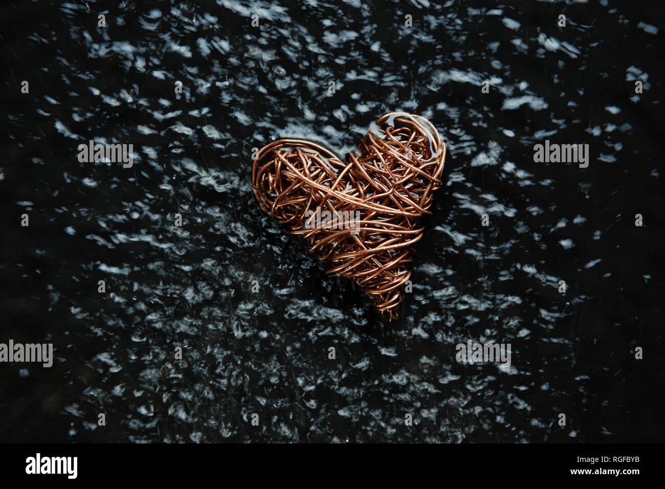 Copper wire heart made from reclaimed electric cable. Light reflections off dense pattern of agitated ripples created by water spray Stock Photo