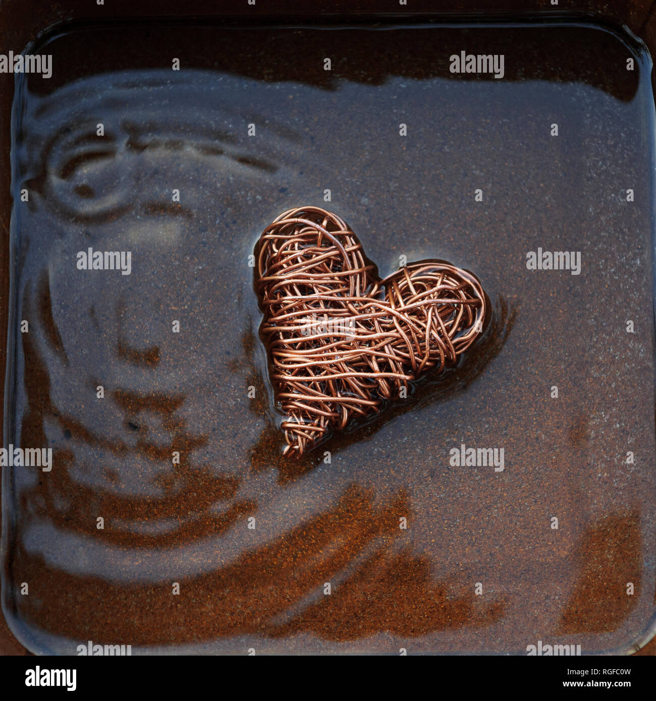 Heart made from copper wire in shallow water with concentric ripples caused by water droplets. Stock Photo