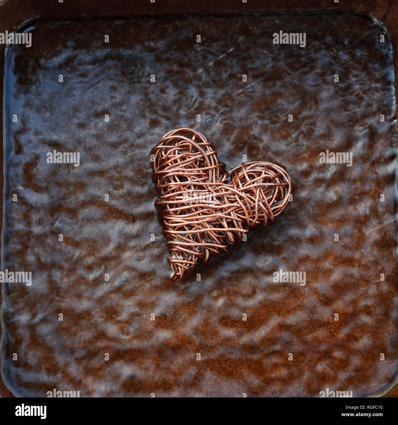 Heart made from copper wire placed in a try of water agitaed to give chaotic ripples. Stock Photo