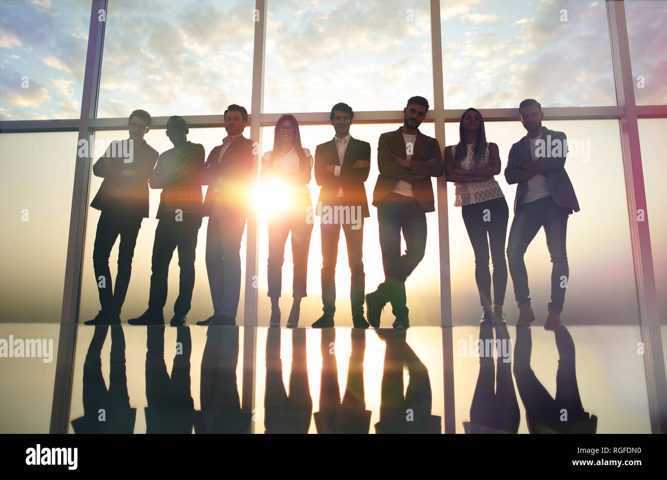 group of young professionals standing in an office with a large window ...