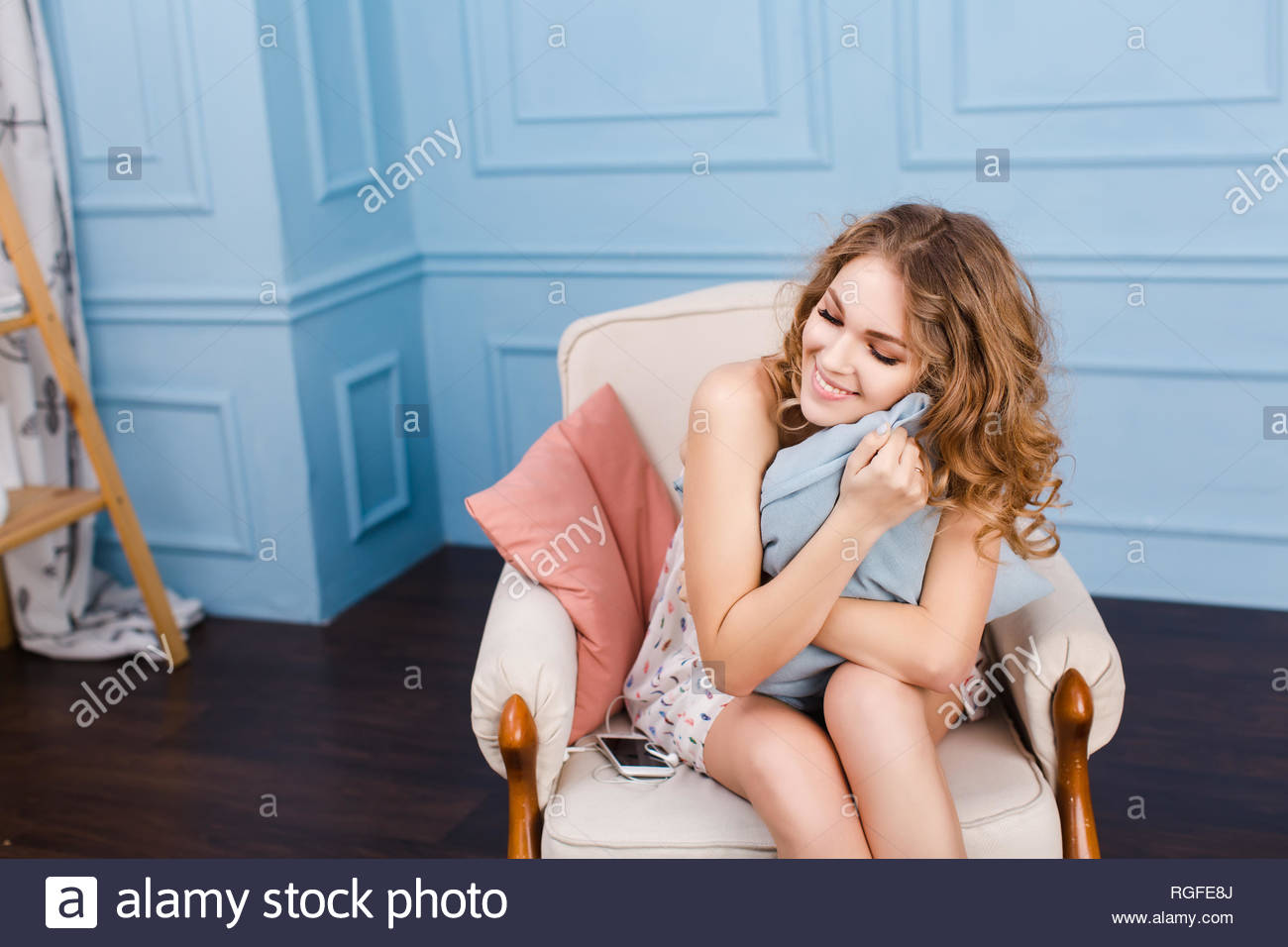 Cute Girl With Blond Curly Hair Sits On Armchair In Studio With