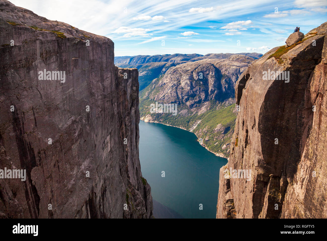 Couple enjoying aerial view of Lysefjord (Lysefjorden) sitting on a boulder at the edge of Kjerag (or Kiragg) Plateau, a popular travel destination in Stock Photo
