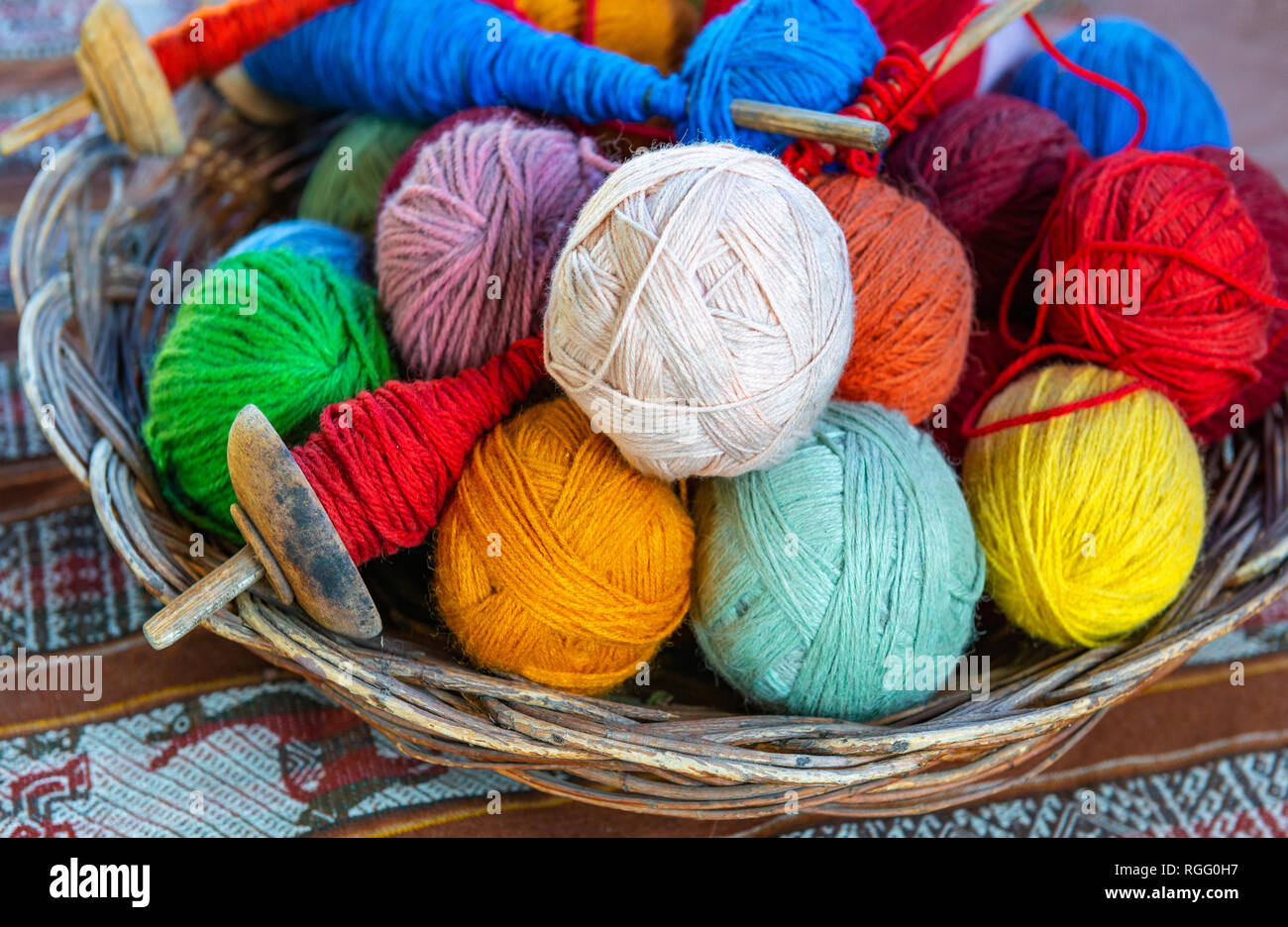 Basket with colourful alpaca wool yarn balls and spinning spindles in a textile production center in Cusco, Peru. Stock Photo