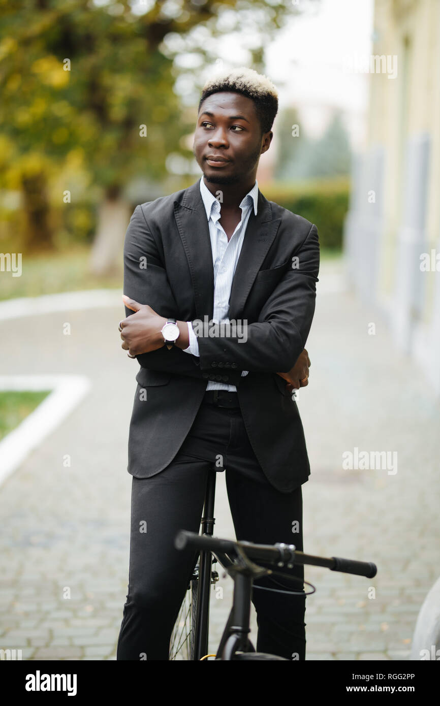 Handsome Afro American man in suit leaning on his bike while standing ...