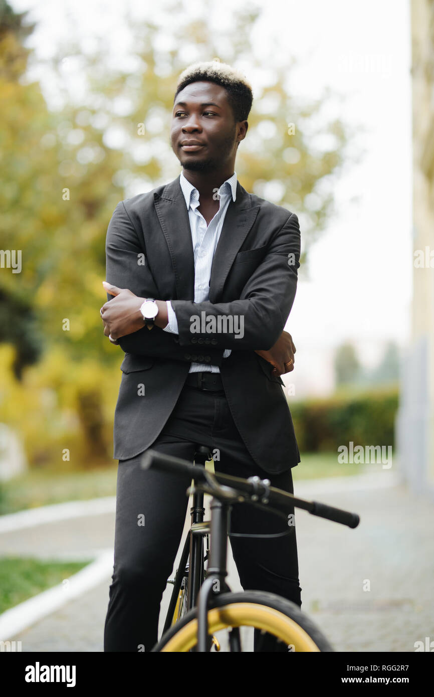 Handsome Afro American man in suit leaning on his bike while standing ...