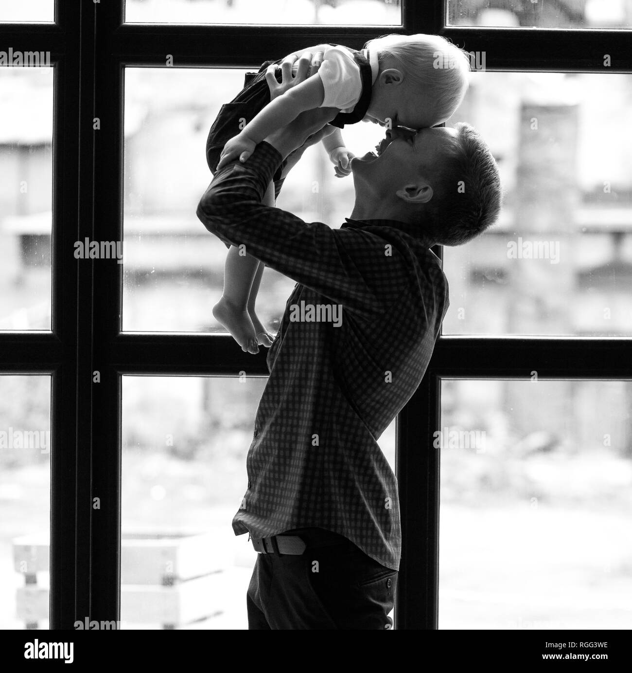 Young father plays with his little son and throws up his against window background. Black and white image. Stock Photo