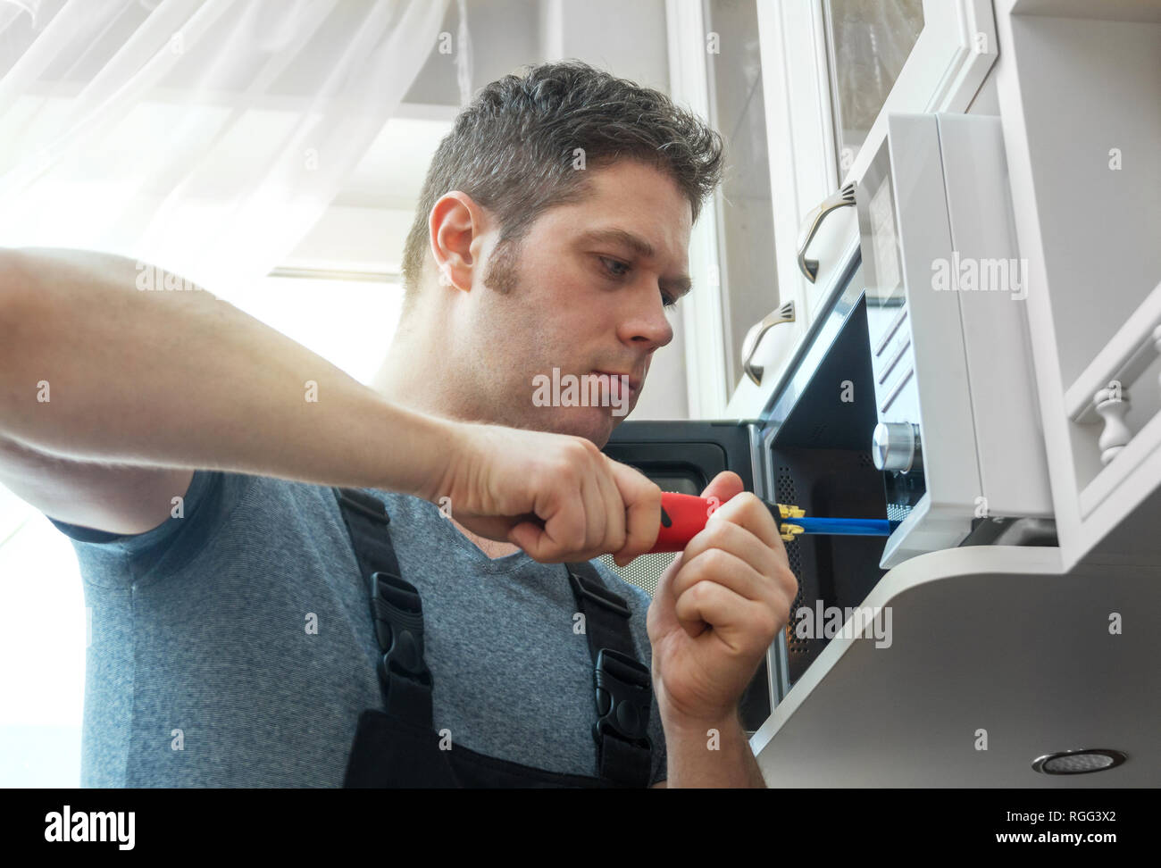 Male technician repairing microwave oven at home. Stock Photo