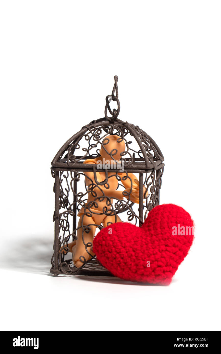 Action figure sitting in cage and there is a red heart on the outside on white background. Concept of Love, imprisonment and deprivation Stock Photo