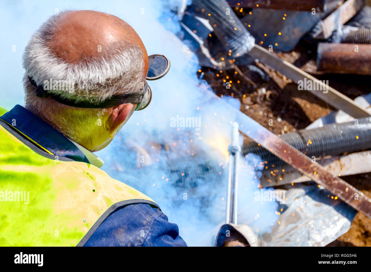 Worker is cutting scrap metal with acetylene torch wearing protective