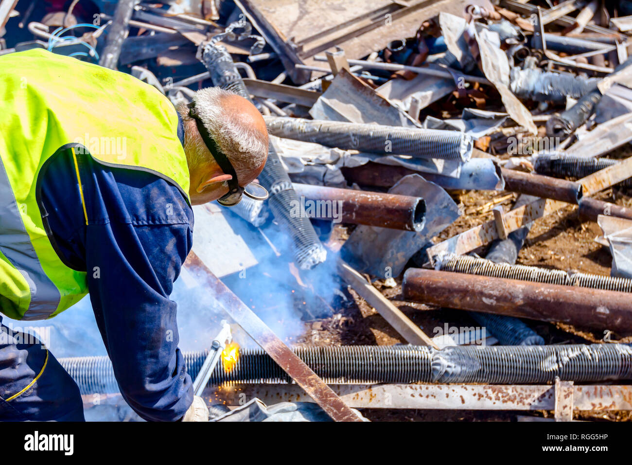 Worker is cutting scrap metal with acetylene torch wearing protective