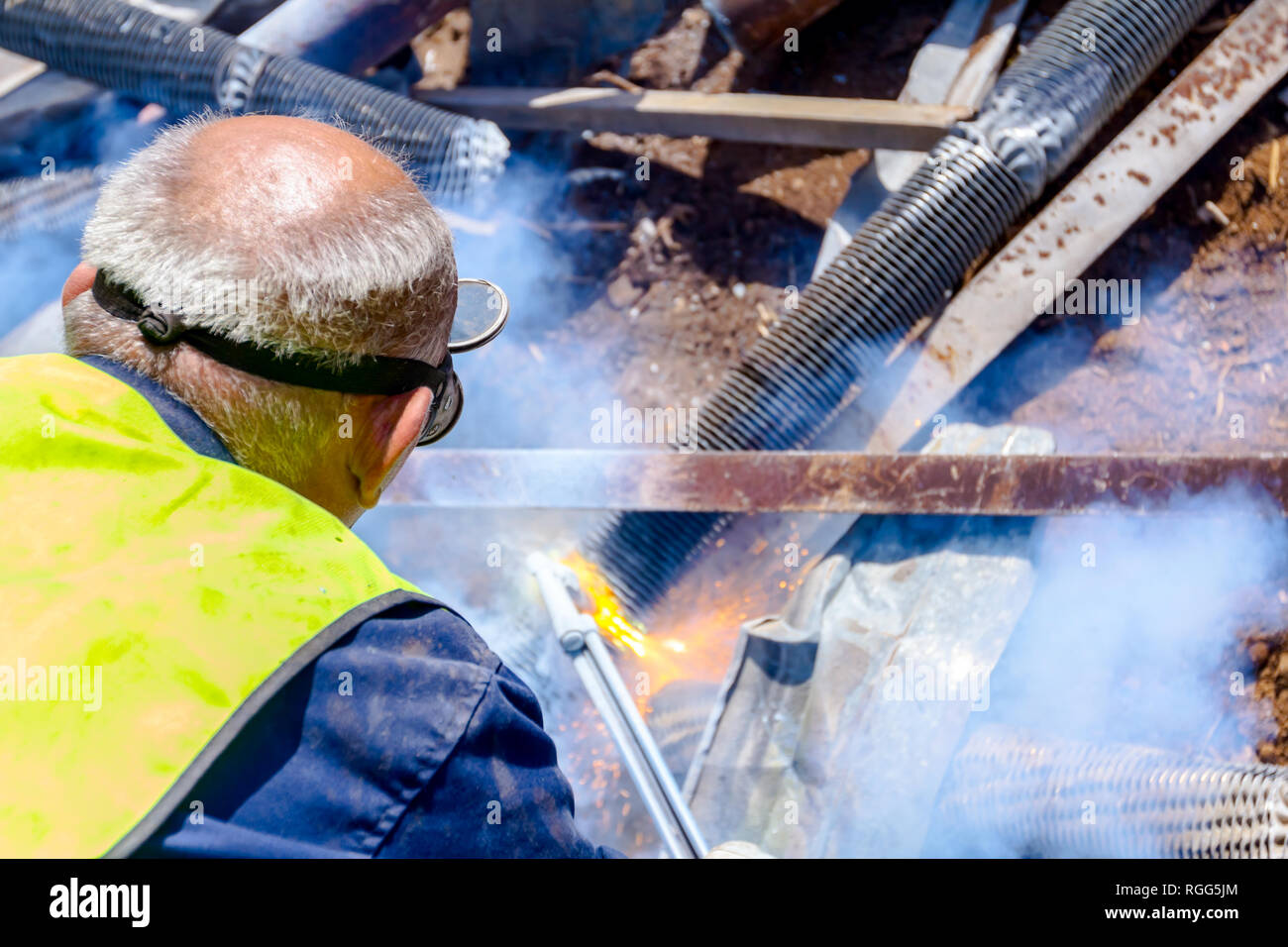 Worker is cutting scrap metal with acetylene torch wearing protective