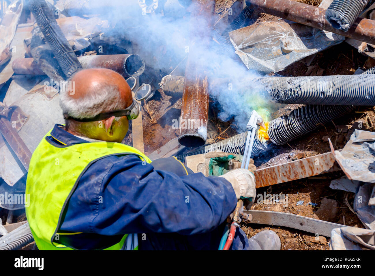 Worker is cutting scrap metal with acetylene torch wearing protective