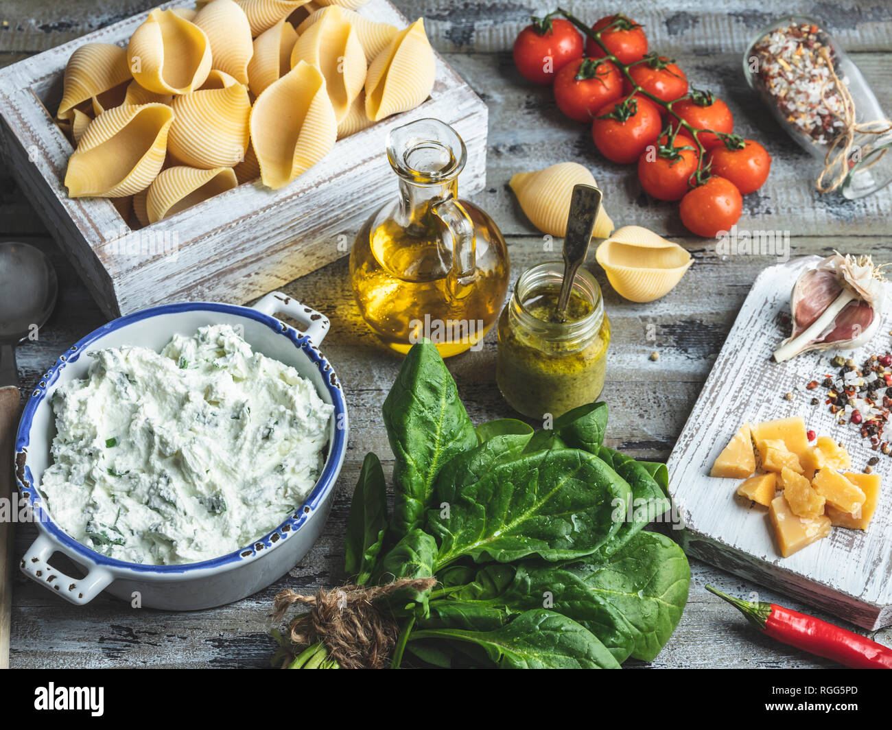 Ingredients for cooking pasta. Conchiglioni, spinach leaves, cherry tomatoes, parmesan cheese, cream cheese, olive oil, salt, garlic, rustic style, wo Stock Photo