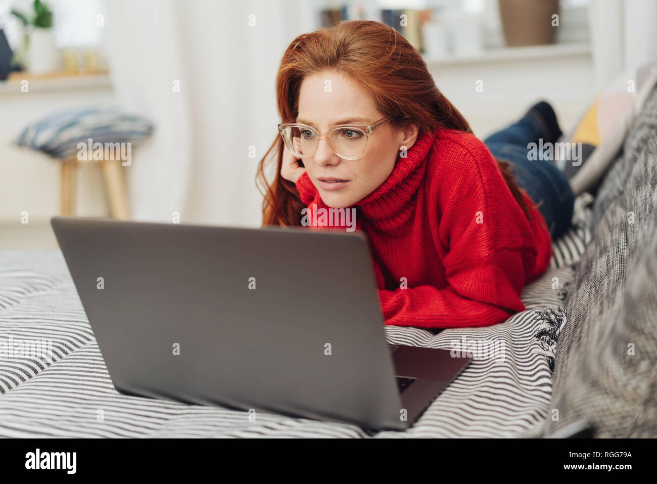Young Woman Using A Laptop On A Sofa As She Relaxes With Her Feet Up 