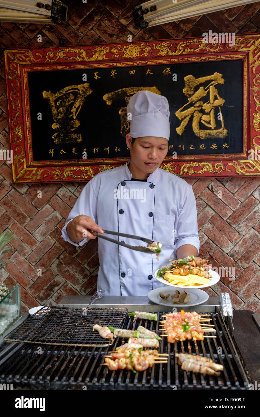 Cook grilling meat and shellfish at a chinese restaurant Stock Photo