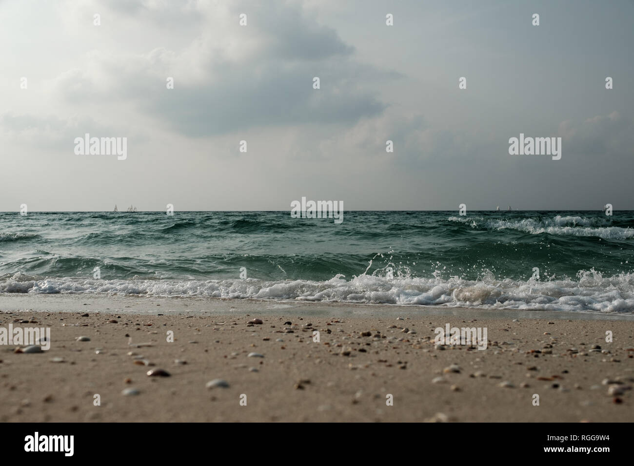 Sailing boats in a distance and waves on the beach, Sharjah, UAE Stock Photo