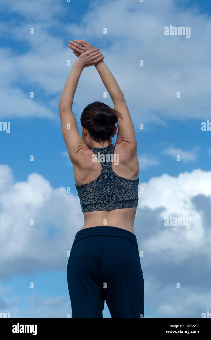 back view of a sportswoman doing an arm stretch outdoors with blue sky background Stock Photo