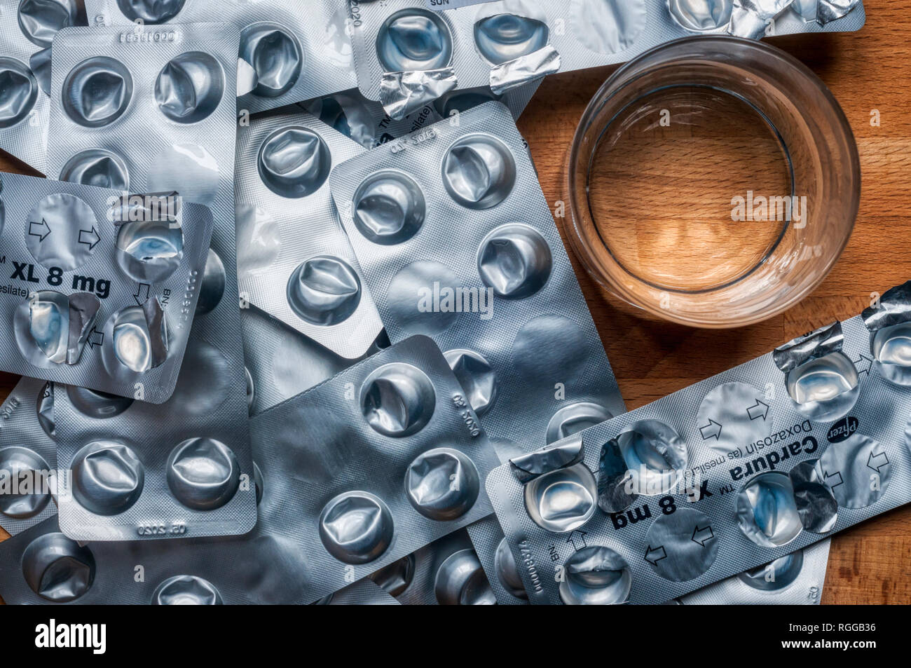 Empty used blister packs of tablets used to control high blood pressure on a bedside table with a glass of water. Medical shortage concept. Stock Photo