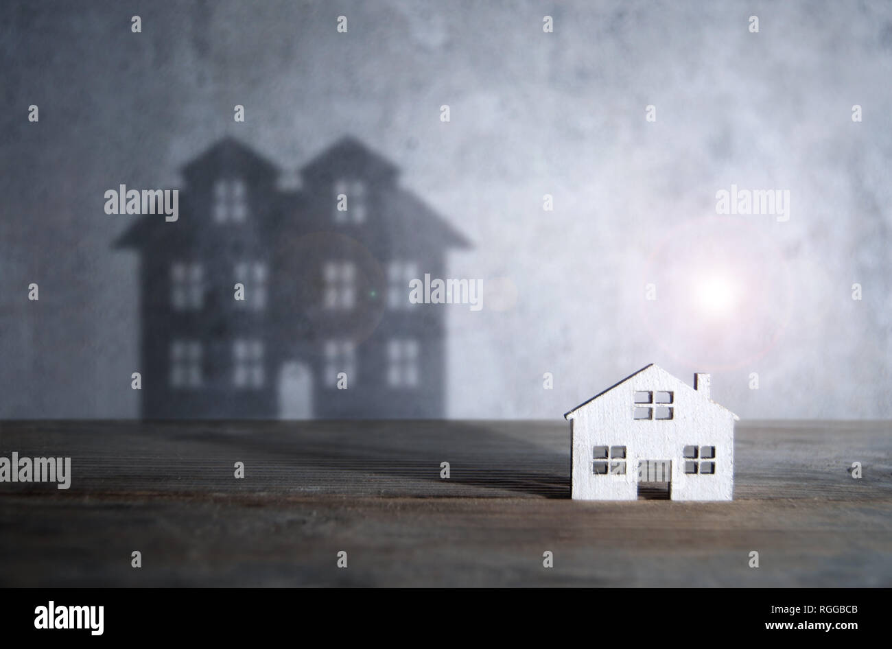 Shadow of a large house emerging from a miniature home Stock Photo