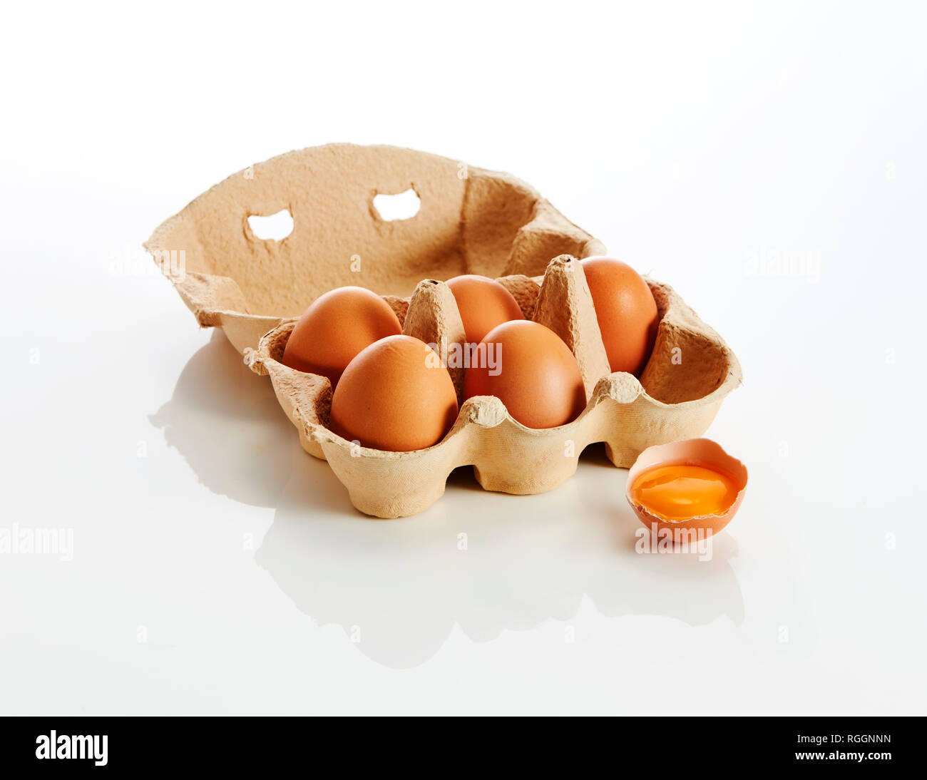 Egg box with brown eggs and an opened egg on white background Stock Photo