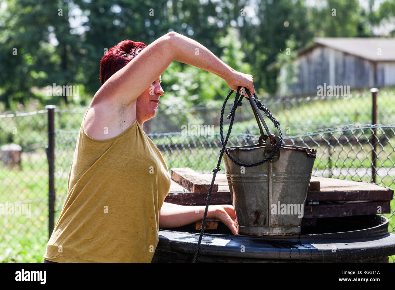 Side view of a woman pulling the bucket from well in one summer day