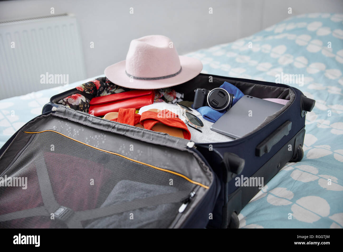 Suitcase with summer vacation utensils on bed Stock Photo