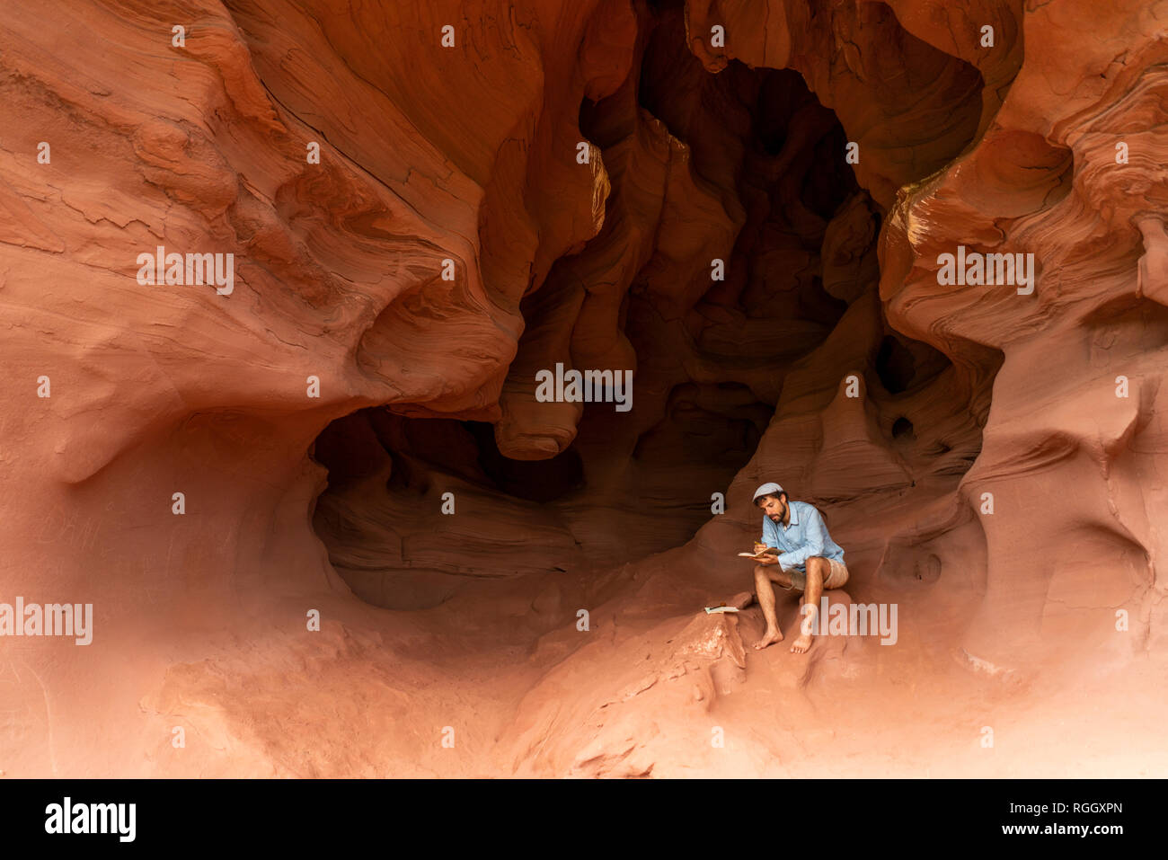 Young man sitting in a cave, taking notes Stock Photo
