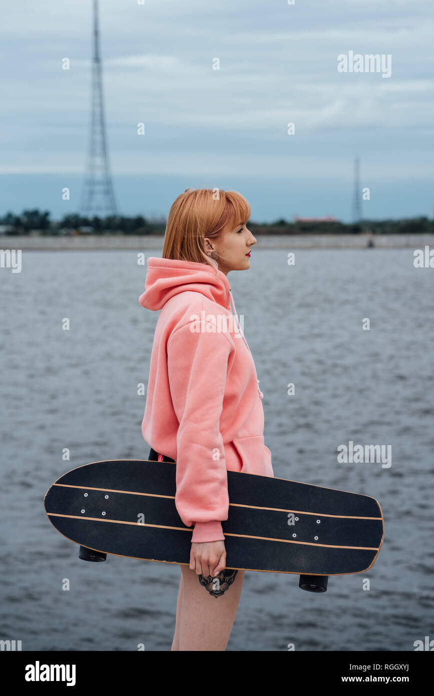 Young woman holding carver skateboard standing at the riverside Stock Photo