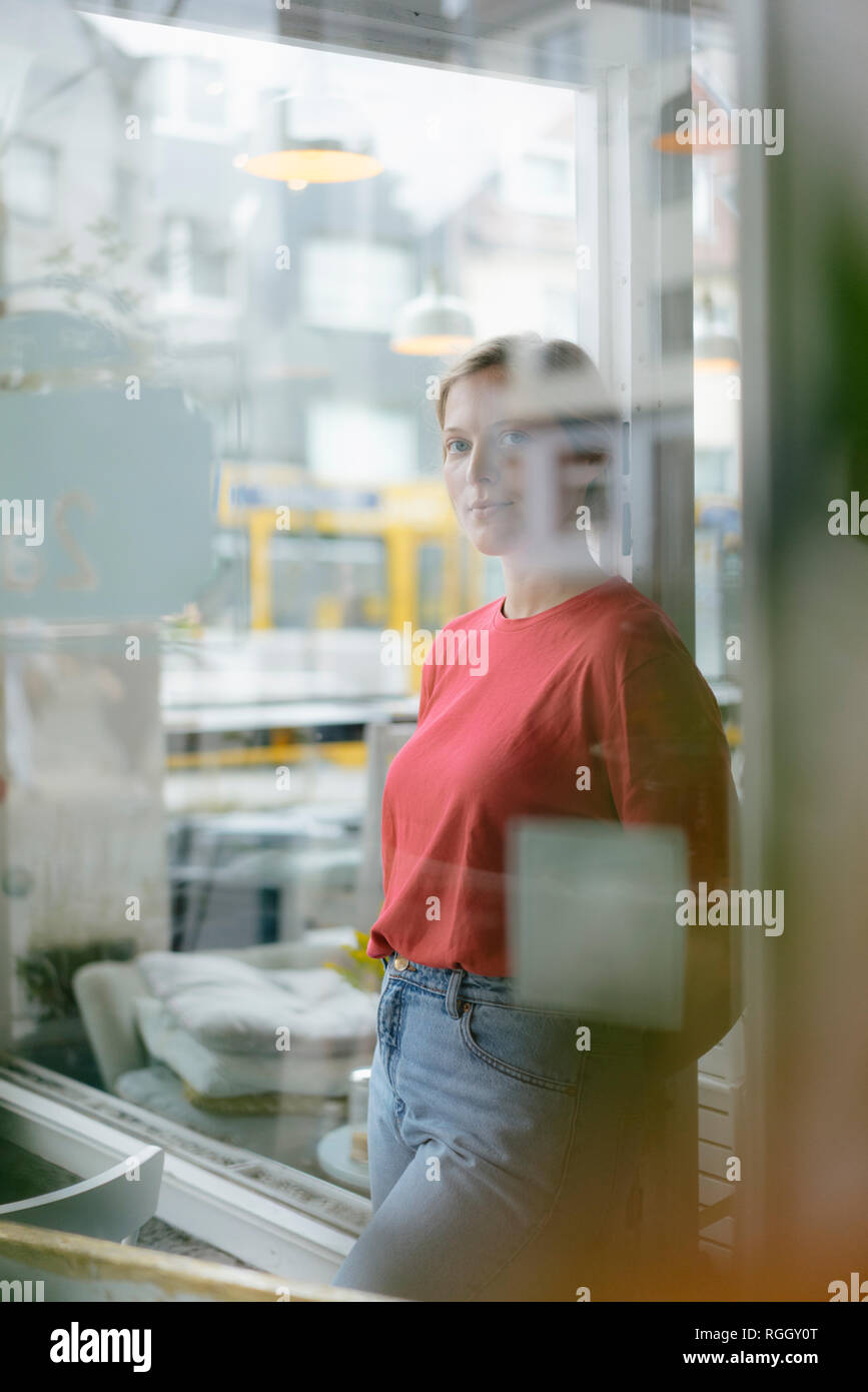 Portrait of young woman leaning against French door in a cafe Stock Photo