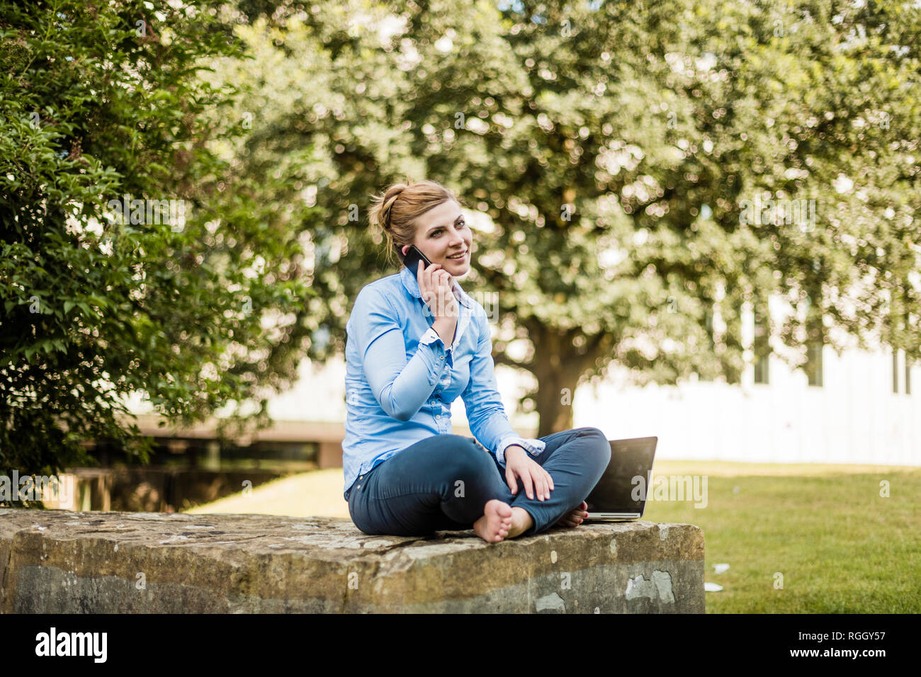 Smiling woman sitting in urban park talking on cell phone Stock Photo