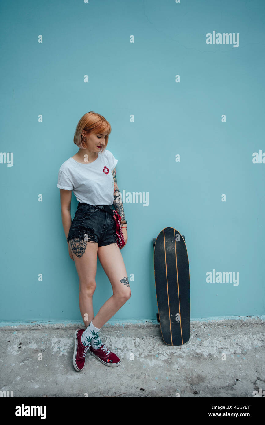 Cool young woman standing at turquoise wall next to carver skateboard Stock Photo