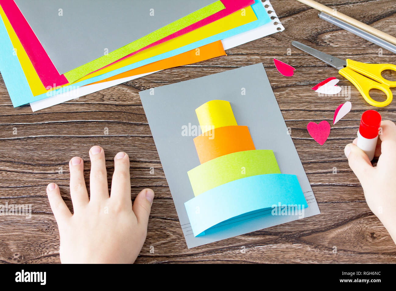 The child cuts out Greeting card with birthday cake congratulation. Children's art project craft for kids. Craft for children. Stock Photo