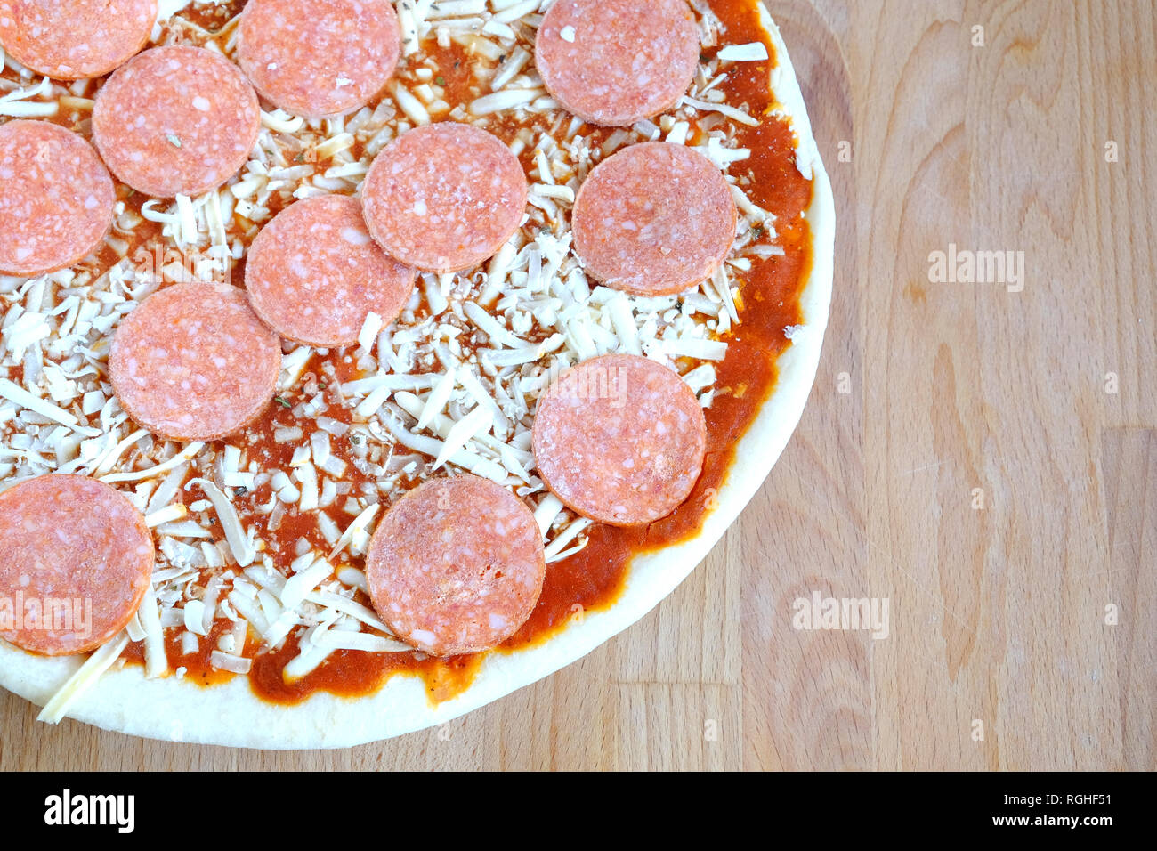 Still life with part of unready pizza with sausage on sandy brown wooden kitchen table top view closeup Stock Photo