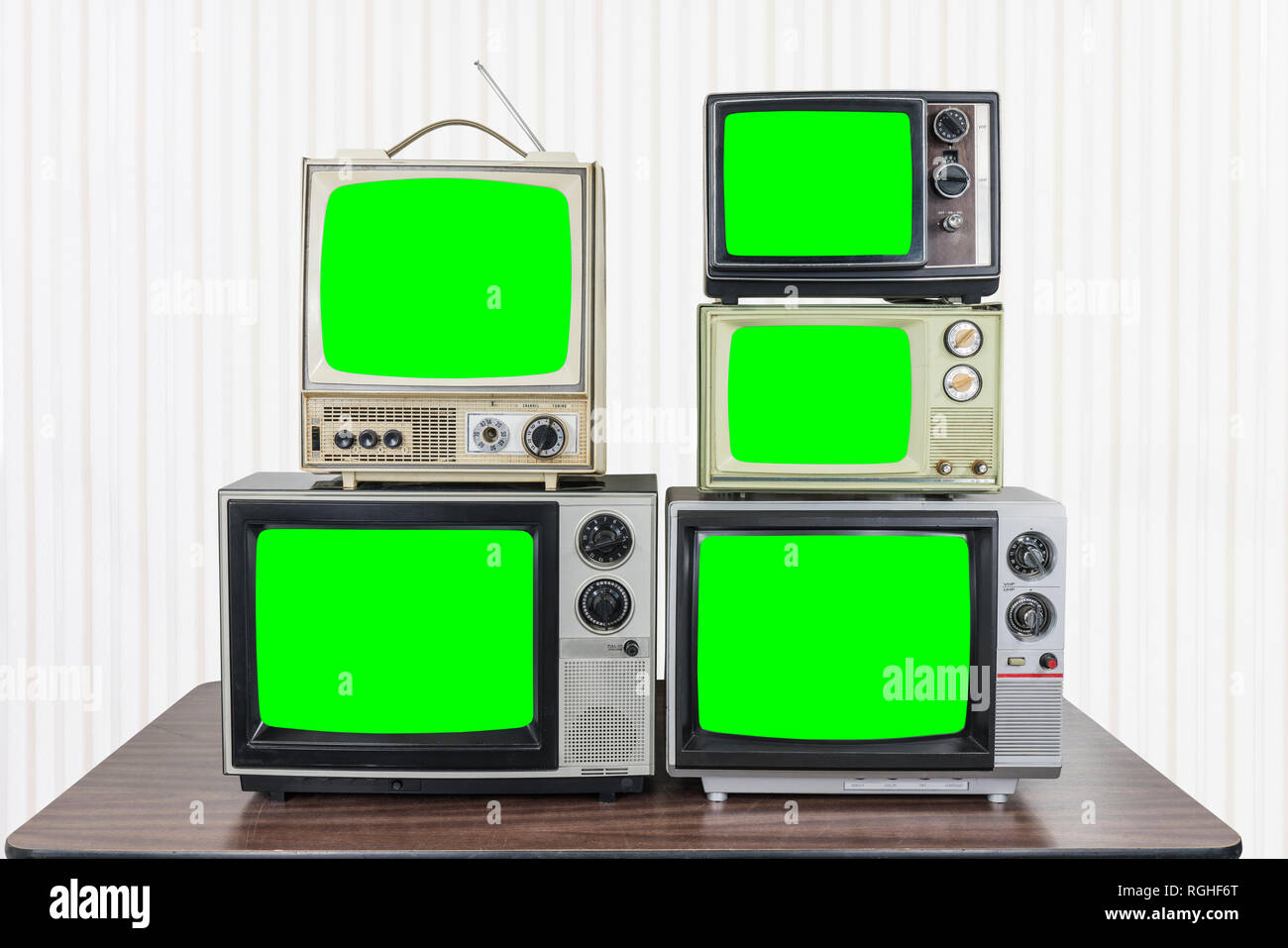 Five vintage televisions on old wood table with chroma key green screens Stock Photo