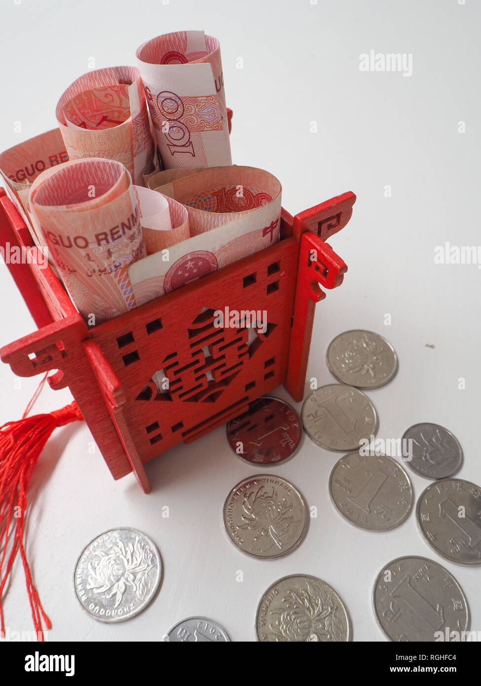 Miniature Chinese pavilion in bright red filled with Chinese 100 renminbi banknotes and surrounded by 1 yuan coins Stock Photo