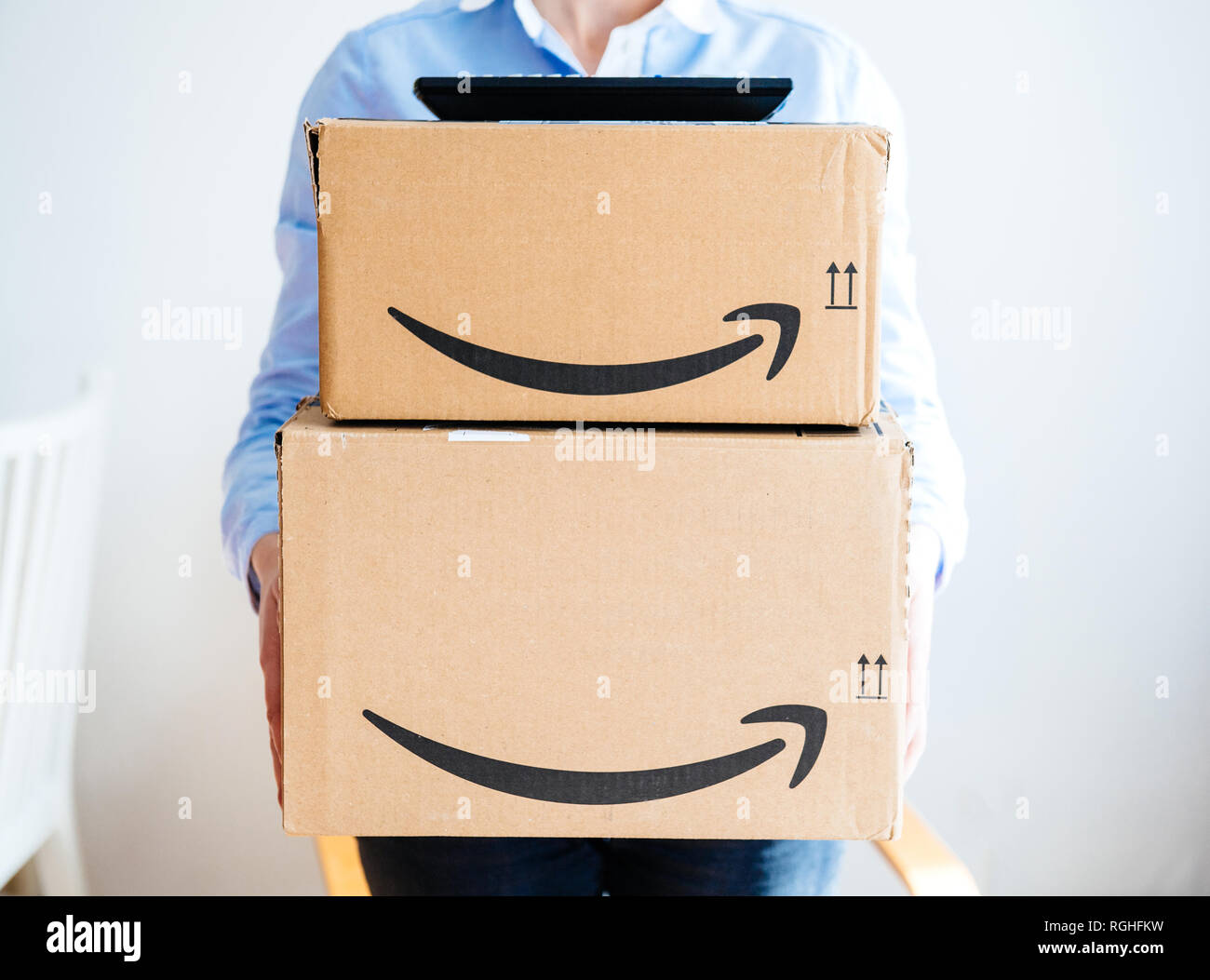 PARIS, FRANCE - MAR 16, 2018: Vie from the front of happy smiling woman holding two large Amazon Prime cardboard boxing after delivery - TV set remote on top on boxes  Stock Photo