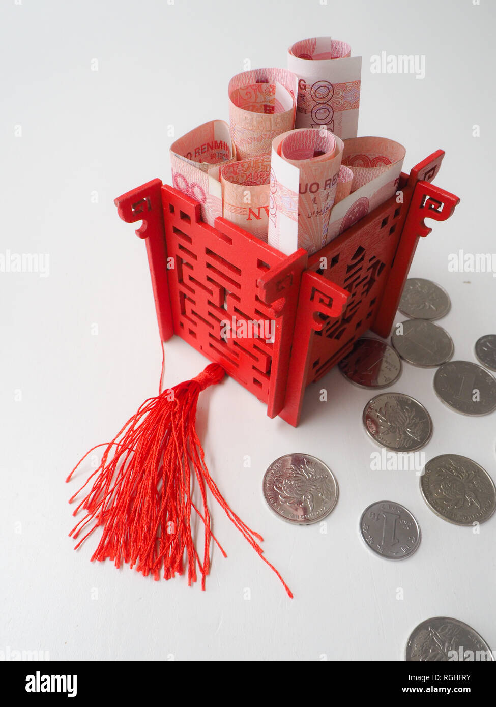 Miniature Chinese pavilion in bright red filled with Chinese 100 renminbi banknotes and surrounded by 1 yuan coins Stock Photo