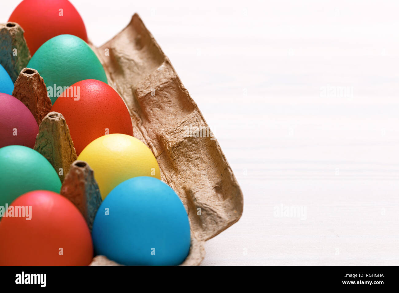 Multi-colored Easter eggs in a box on a white table. Copy space Stock Photo