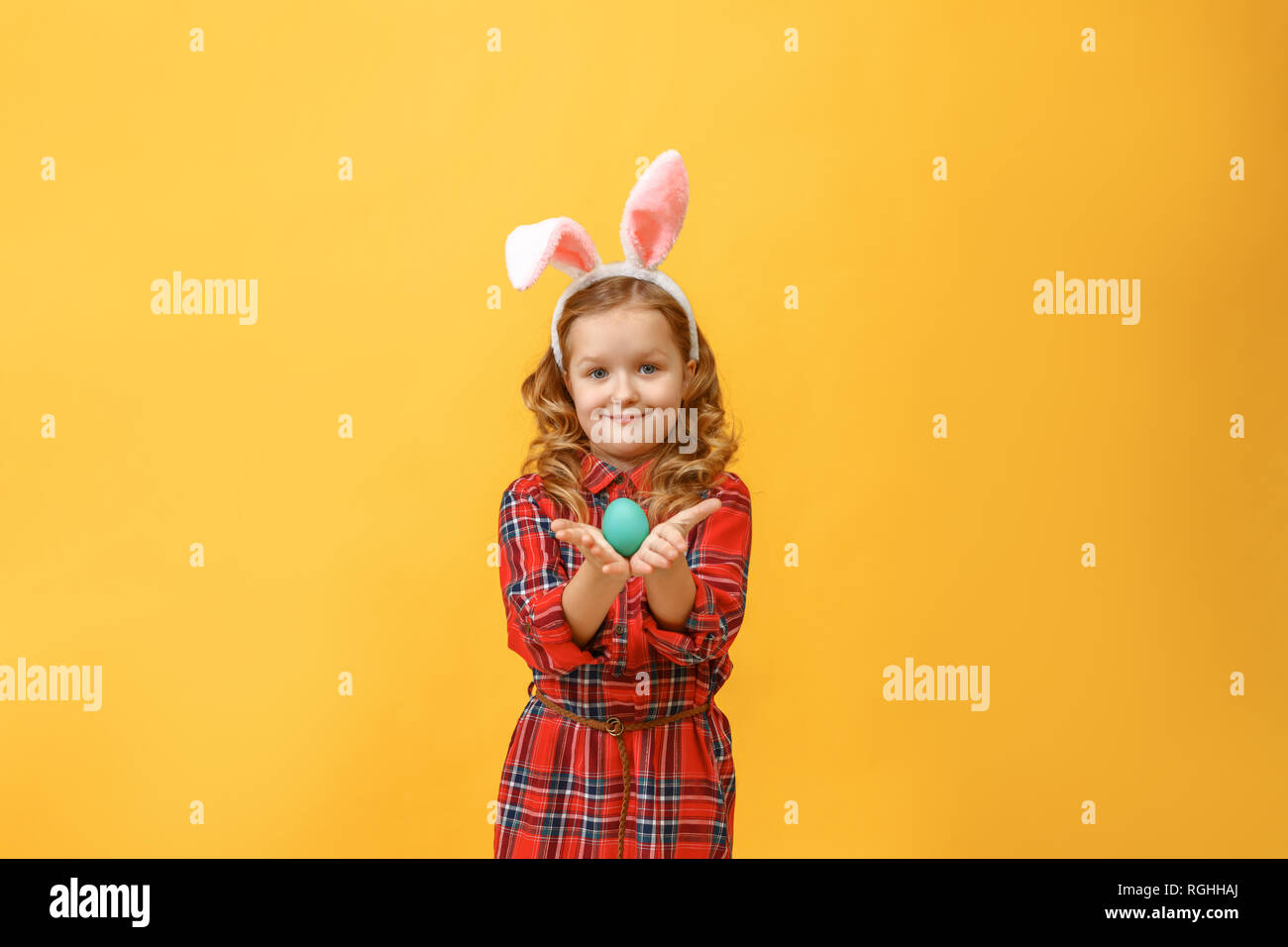 Cheerful little kid girl with bunny ears with an easter egg on a colored background. Stock Photo