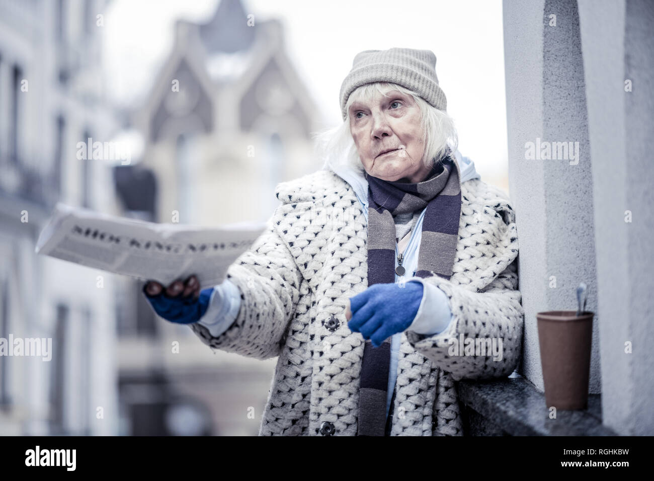 Cheerless aged woman offering newspaper to people Stock Photo