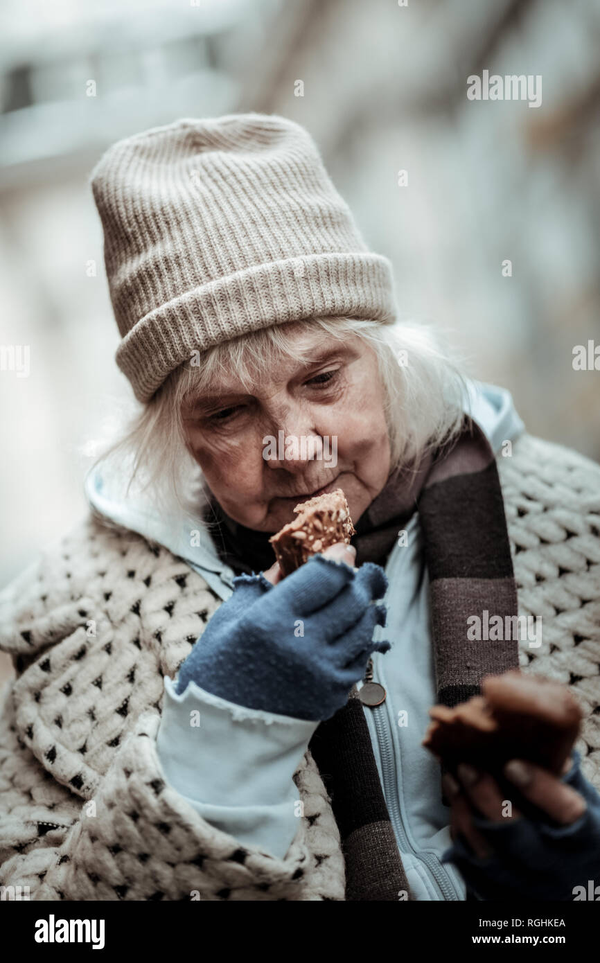 Unhappy homeless woman eating a piece of bread Stock Photo