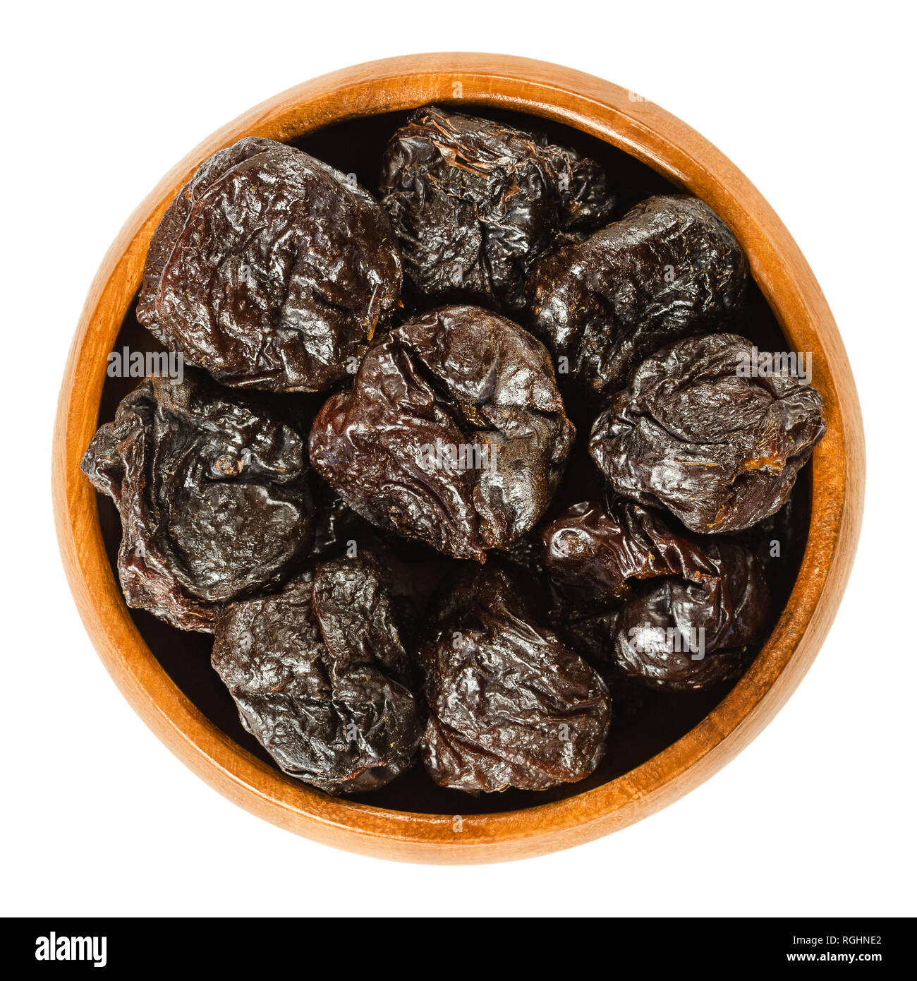Prunes, dried plums in wooden bowl. Uncooked, dehydrated, pitted fruits of Prunus domestica with black color, used as snack. Isolated macro photo. Stock Photo