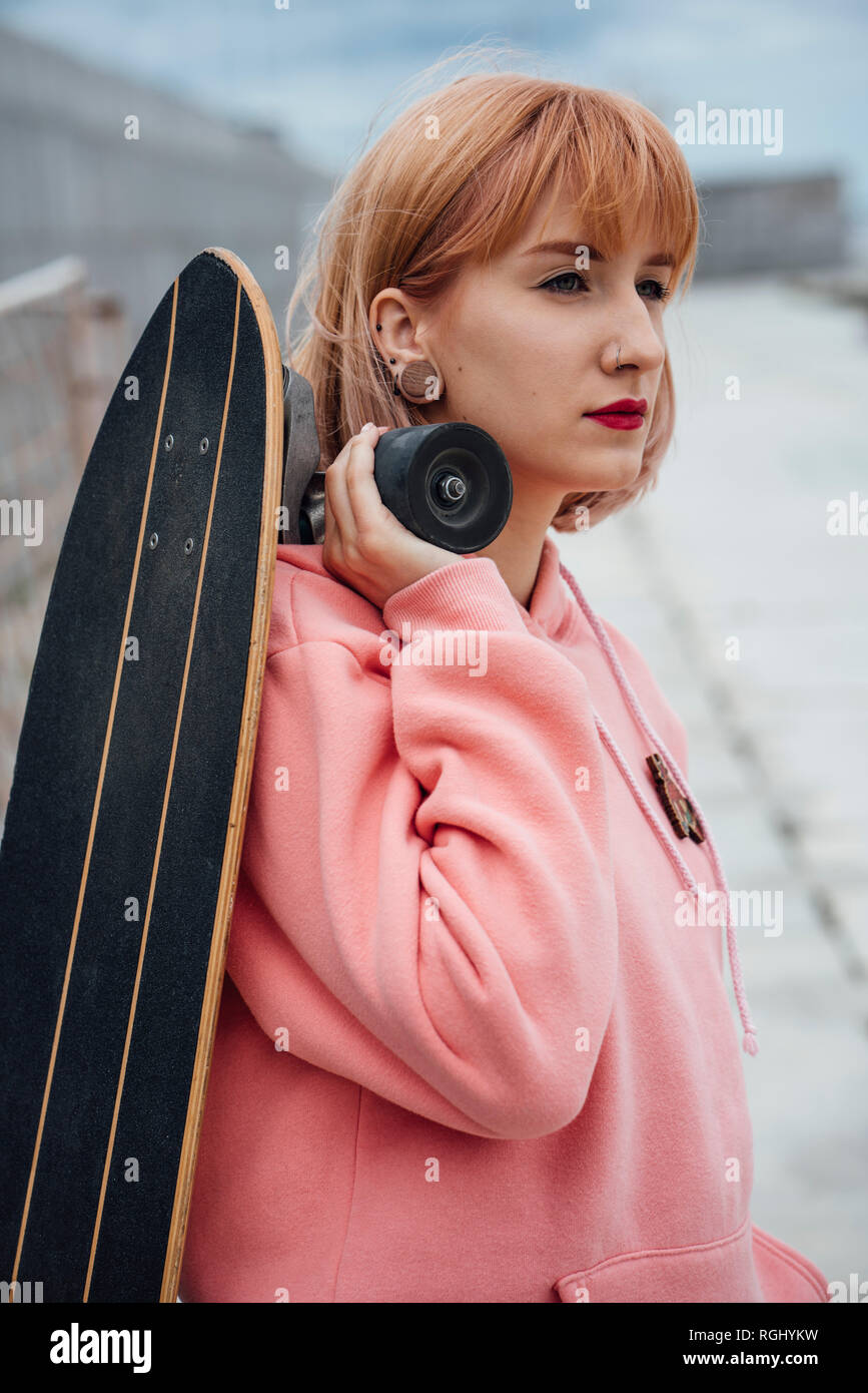 Cool young woman holding carver skateboard outdoors Stock Photo