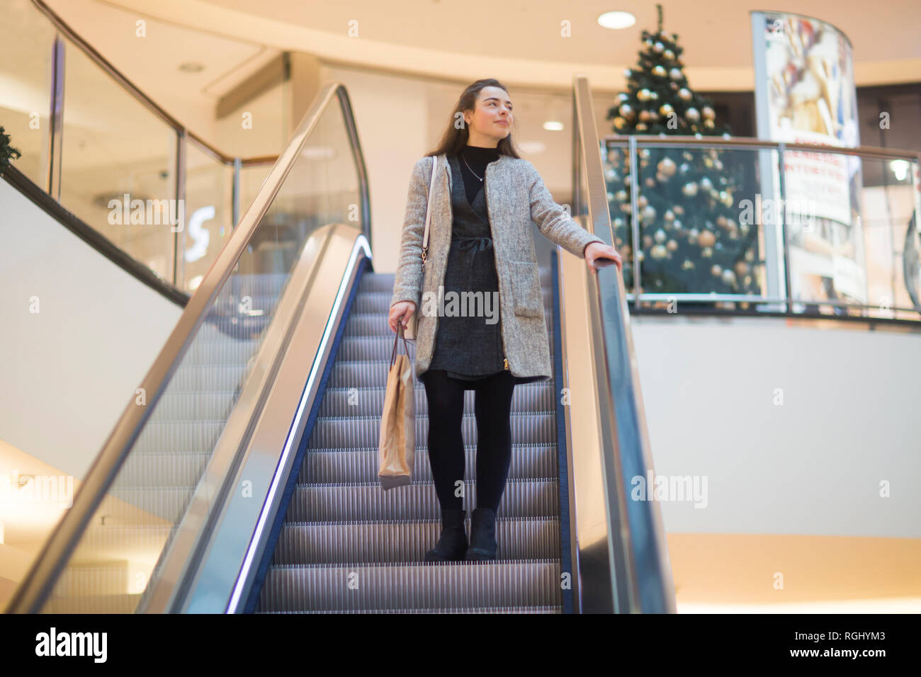 Young woman with shopping bag standing on escalator in a shopping mall at Christmas time Stock Photo